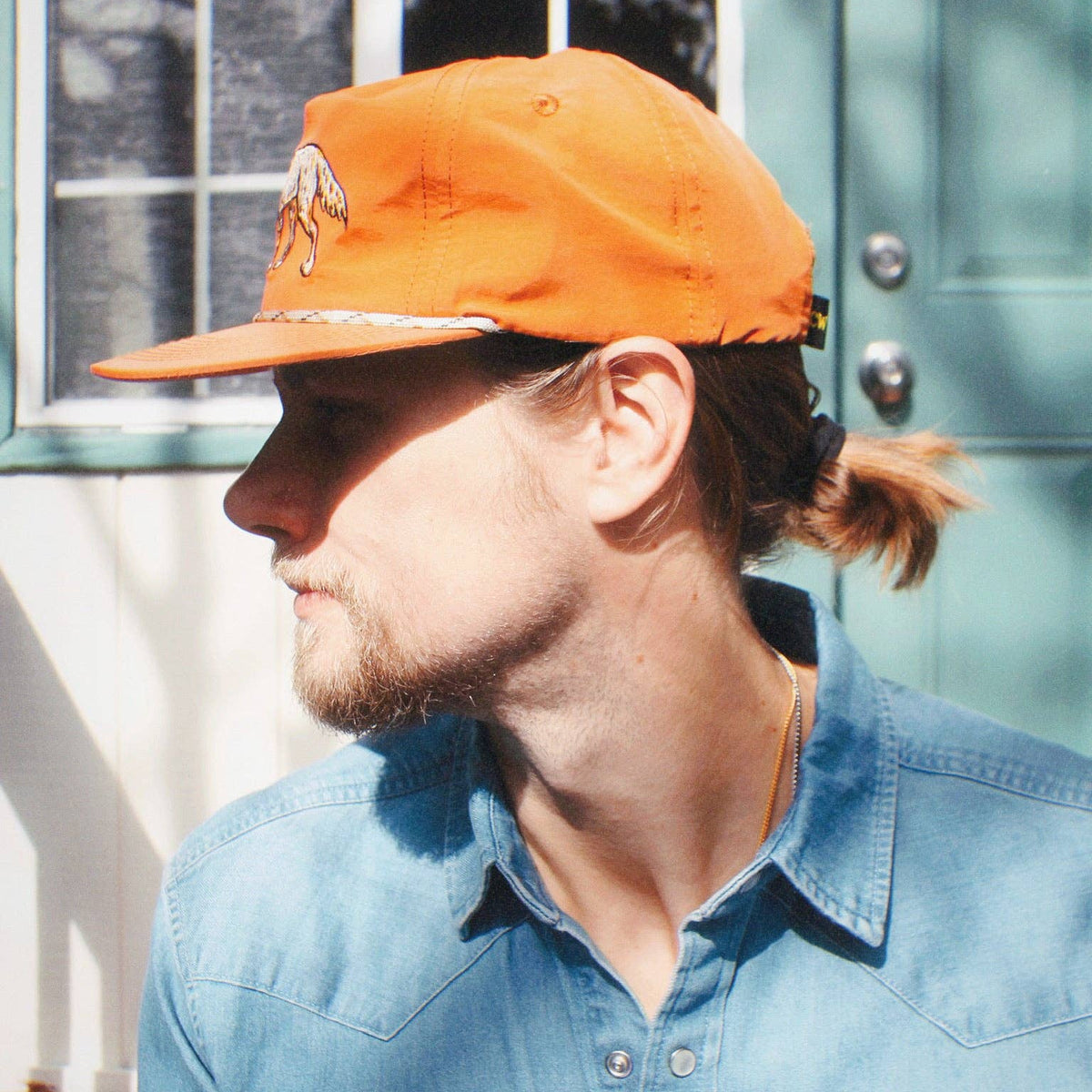 Back view of a person wearing the orange coyote hat with ponytail visible and denim shirt