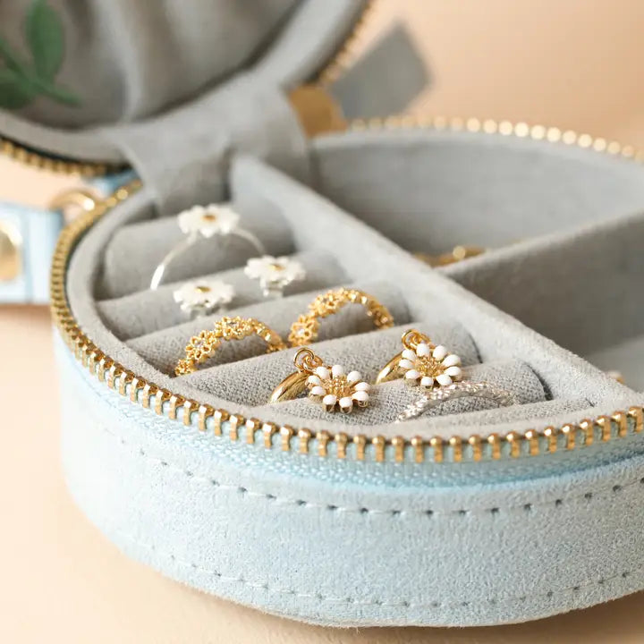 Open round velvet jewelry case showing gold rings with white flower accents in the soft gray interior.