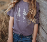 Girl wearing a purple Wild and Free kids tee with white botanical graphic