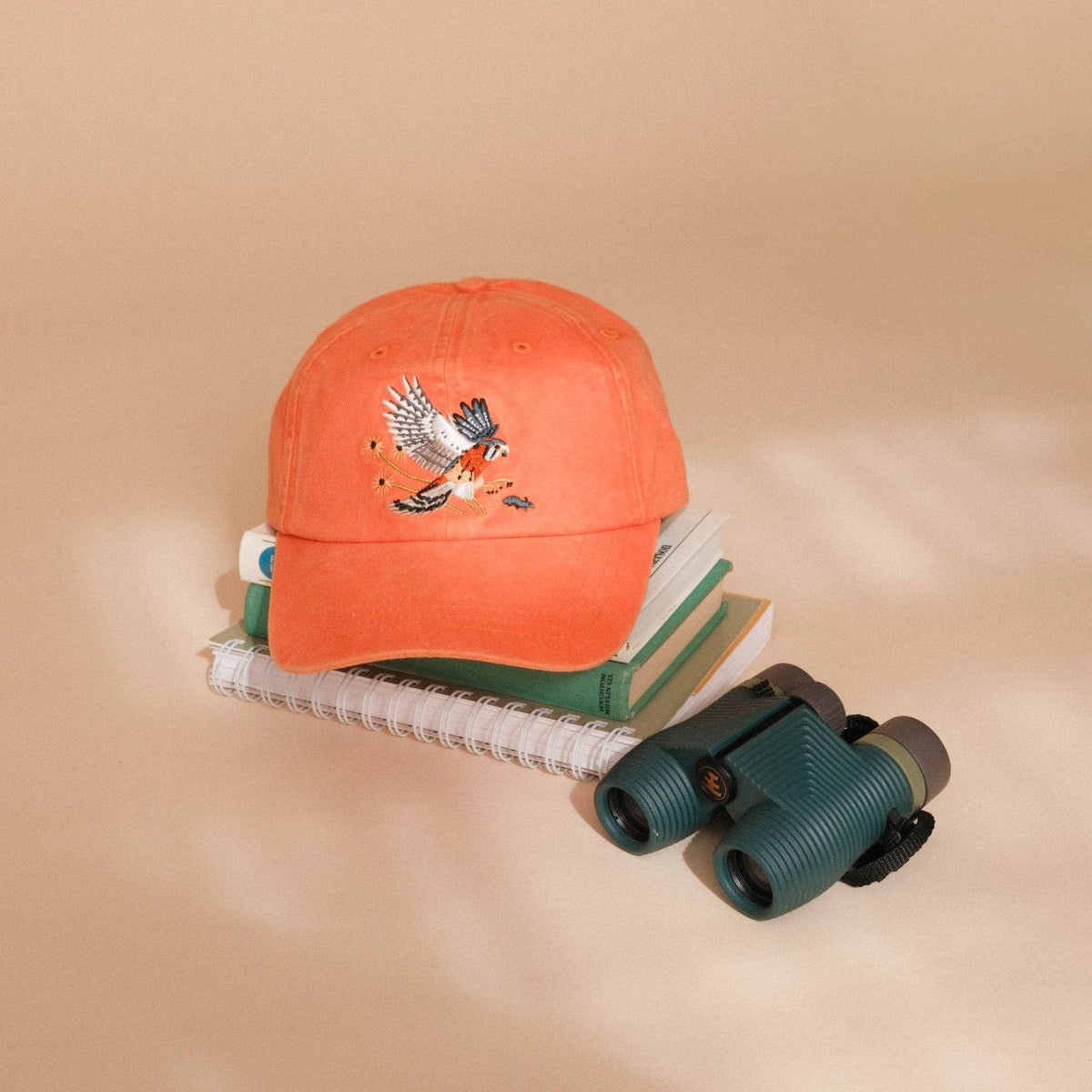 Orange Washed Dad Hat resting on a stack of books with a front panel embroidered bird in flight