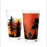 Two pint glasses featuring silhouetted trees and a Bigfoot figure against an orange sunset.