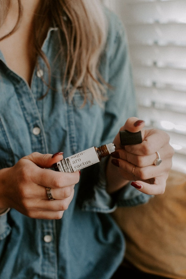 Hands hold a Saguaro Roll-On Perfume bottle with its label visible