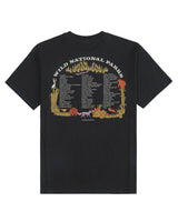 Back view of a black Peaceful Parks Tee with a large arch graphic of trees and desert flora.