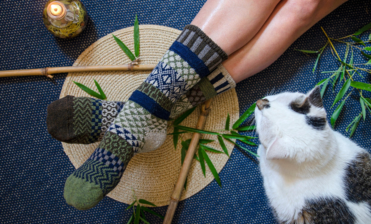 Legs wearing blue gray striped bamboo wool crew socks on a blue rug with a white and brown dog nearby