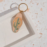 Cactus enamel keychain with green cactus on a peach sunburst background attached to a gold ring