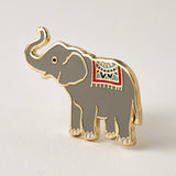 Close up of a gray elephant enamel pin with gold edges and a colorful decorative saddle cloth.