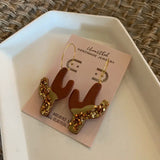 Copper State saguaro dangle earrings featuring brown cactus shapes and gold hammered accents on a pink display card.