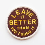 Circular maroon embroidered patch with yellow text Leave It Better Than You Found It and a white stitched edge.
