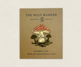 Red mushroom enamel pin attached to The Wild Wander packaging card on brown cardboard