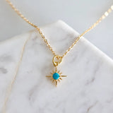Gold chain necklace with turquoise round center and sunburst star pendant on a marble surface