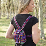 Colorful woven mini backpack with purple and red stripes worn over a black shirt in a park