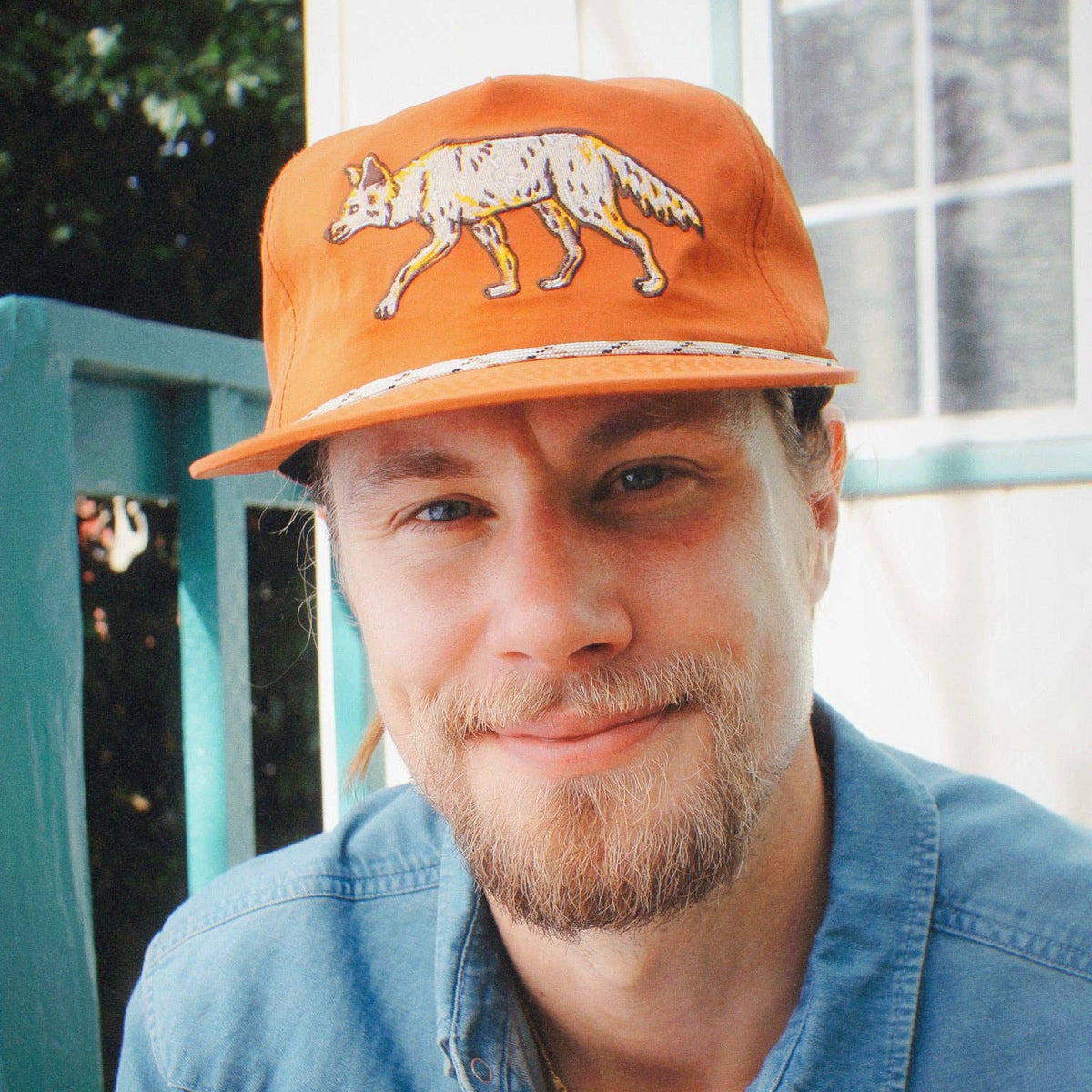 Side profile of a man wearing orange coyote hat with walking coyote embroidery, paired with a blue denim shirt