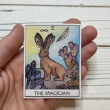 Tarot card The Magician depicting a desert scene with a rabbit and purple crystals