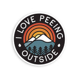 Round sticker showing mountains, pine trees, and a sunset rainbow with I LOVE PEEING OUTSIDE around the border
