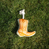 Orange cowboy boot dog toy with white rope loop on green grass