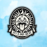 It's a Dry Heat sun sticker showing a cartoon sun with a tongue sticking out and a banner reading It's a Dry Heat.