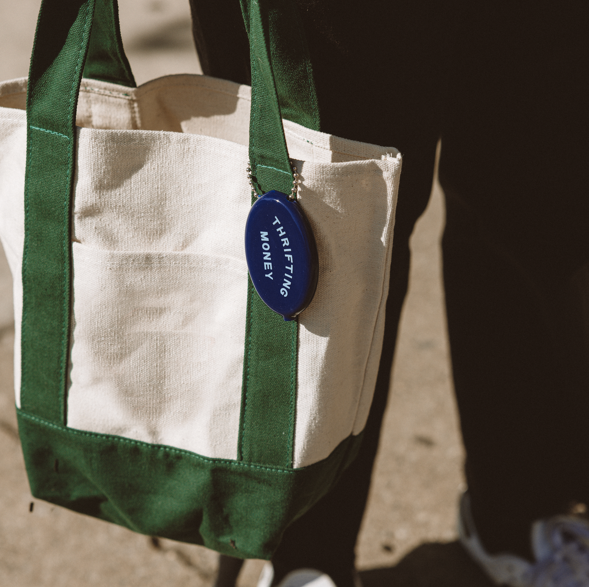 Beige canvas tote with dark green straps and a blue round thrift money tag attached.