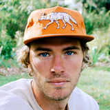 Orange cap with a white embroidered coyote on the front worn by a man outdoors