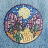Circular desert night patch with purple rock formations, green cacti, a yellow moon, and GET LOST text