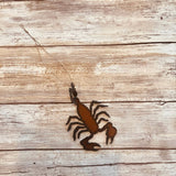 Rusty scorpion metal ornament hanging from twine on weathered wooden background