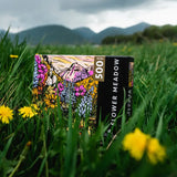 Flower Meadow 500 piece puzzle box resting in green grass among yellow flowers.
