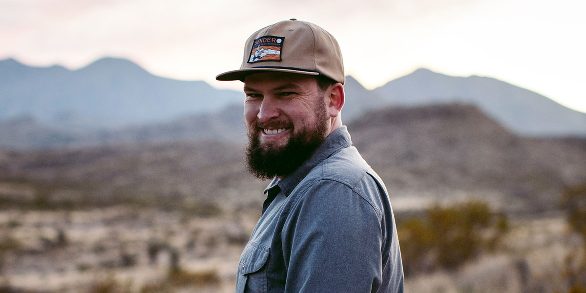 Man wearing a cap with a desert landscape and mountains in the background