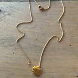 Gold Monstera leaf pendant on a delicate gold chain laid on wood surface