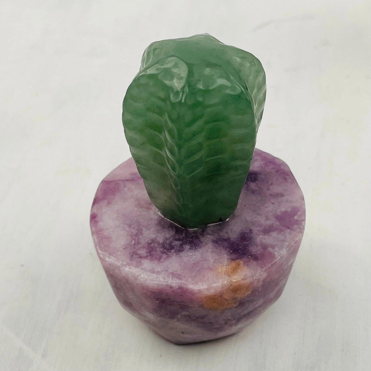 Teal carved crystal succulent atop a purple base.