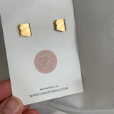 Two gold mirror stud earrings on a white display card with a pink circular plant logo