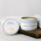 Desert Monsoon 4 oz candle in a pale blue tin with lid off, white label shows a desert plant illustration.