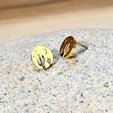 Gold round stud earrings with cactus silhouettes and star cutouts on a textured stone surface