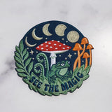 Circular embroidered patch See The Magic Patch depicting a night scene with mushrooms, a frog and foliage.