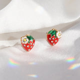 Pair of strawberry enamel stud earrings with green leaves, white flower, and rhinestones on red fruit.