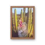 Framed art print of a woman in a pink swimsuit sitting inside a giant glass of ice among desert cacti.