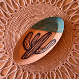 Oval saguaro cactus ceramic tray with turquoise rim resting on a woven circular jute placemat