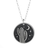 Round silver pendant showing a cactus under a night sky with a crescent moon and stars