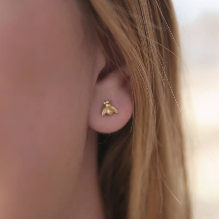 Close-up of a gold bee stud earring worn on a model's ear