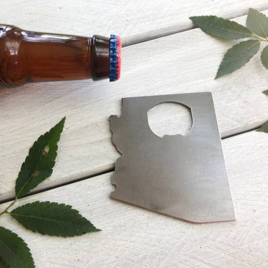 Arizona state shaped steel bottle opener resting on a wooden surface beside a beer bottle