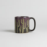Purple glazed round stoneware mug with green cactus silhouettes wrapping around the body.