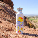 White steel water bottle featuring a colorful desert mural with a bright orange sun and blue mountains.