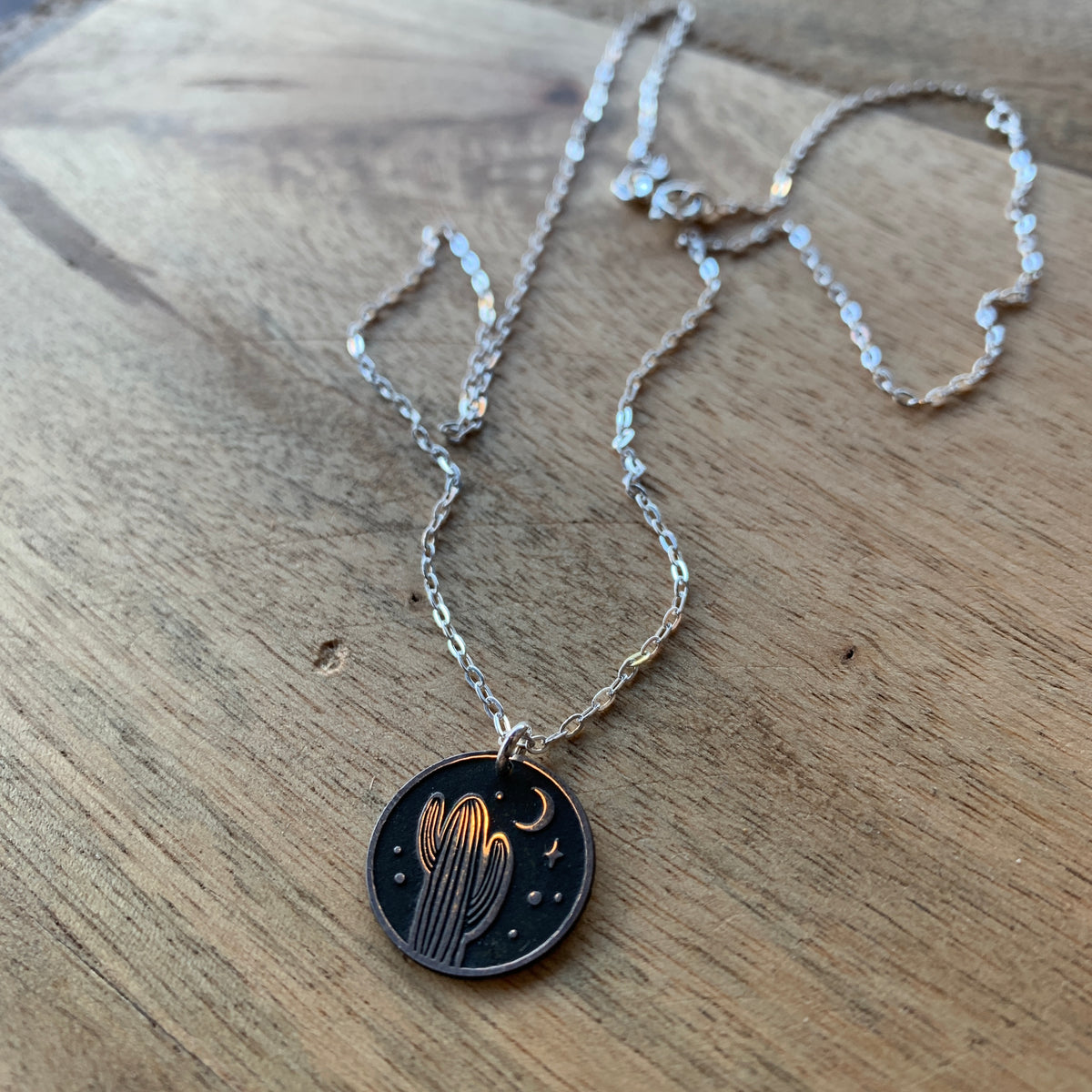 Desert Night Round Necklace close up on a rustic wood surface showing a silver chain and circular pendant.