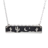Cactus Night Necklace pendant with silhouetted cacti and a crescent moon on a dark desert night.
