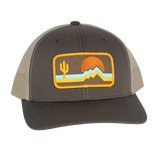 The Retrozona Trucker hat in brown front panel with beige mesh and a desert patch with cactus mountains and sunset.