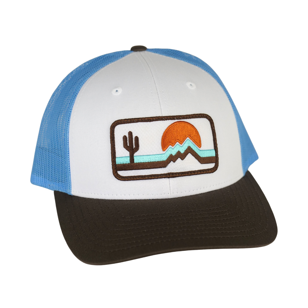 The Retrozona Trucker cap white front panel blue mesh with a desert patch showing cactus mountains and orange sun