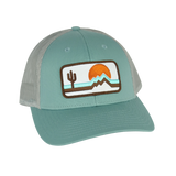 The Retrozona Trucker hat in mint teal with white patch showing a desert scene cactus mountains and sunset.