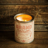 Grand Canyon National Park candle in a metal tin with a vintage pink label and two wicks lit on a wooden surface.