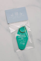 Teal Desert Dreamer hotel key tag with 001 and sun desert illustration in a clear bag with a gold key ring