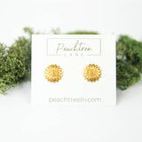 Gold sunflower stud earrings on a white display card.