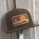 Close up of embroidered desert patch on the brown front of the hat showing cactus and mountains